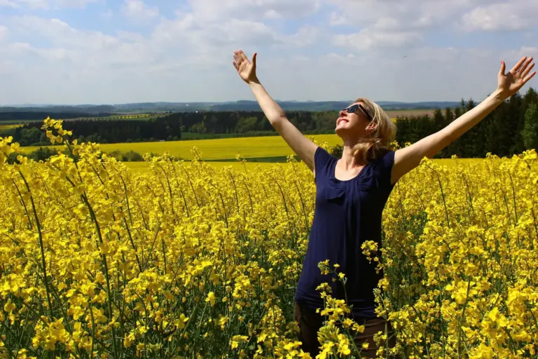 Dankbarkeit im Alltag: eine Frau reißt die Arme hoch auf einem Feld voll gelb blühender Blumen